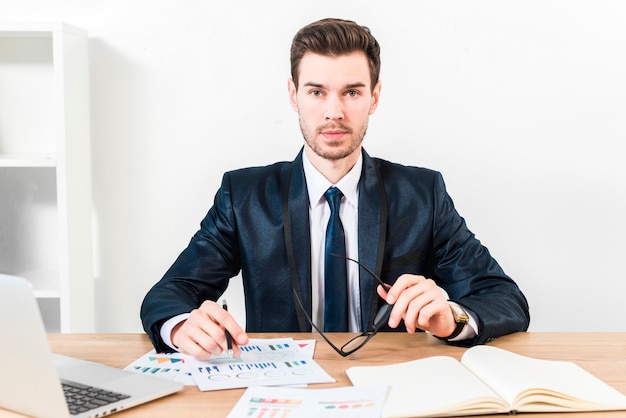 portrait-young-businessman-holding-pen-graph-eyeglasses-hand-looking-camera_23-2148087128